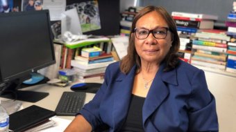 An Aboriginal woman wearing glasses sits at a desk in an office