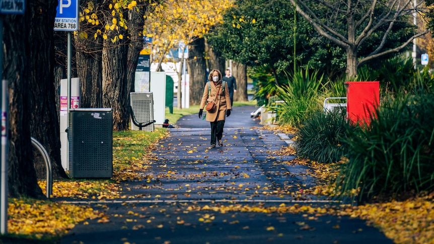 A woman walks down a rainy street wearing a coat and mask.