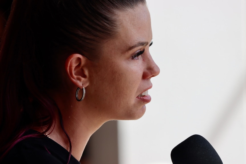 A close-up, side-on shot of a woman addressing a crowd.