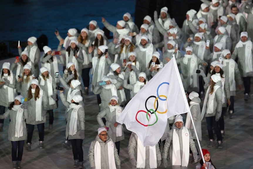 Wide shot of a large group of grey-clad athletes walking into a stadium.
