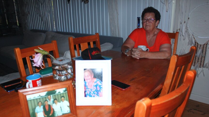 Jocelyn Owers sits at a table with a cup of tea with photo frames in the foreground.