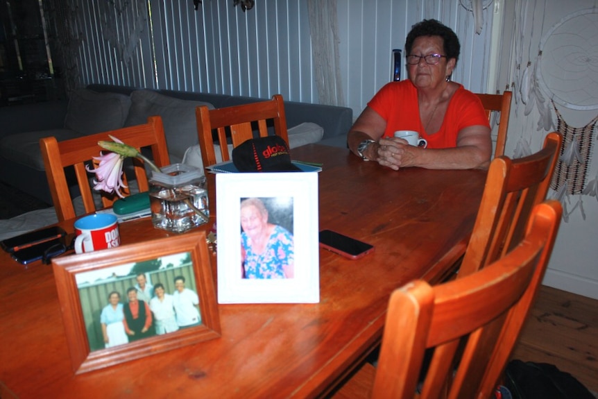 Jocelyn Owers sits at a table with a cup of tea with photo frames in the foreground.