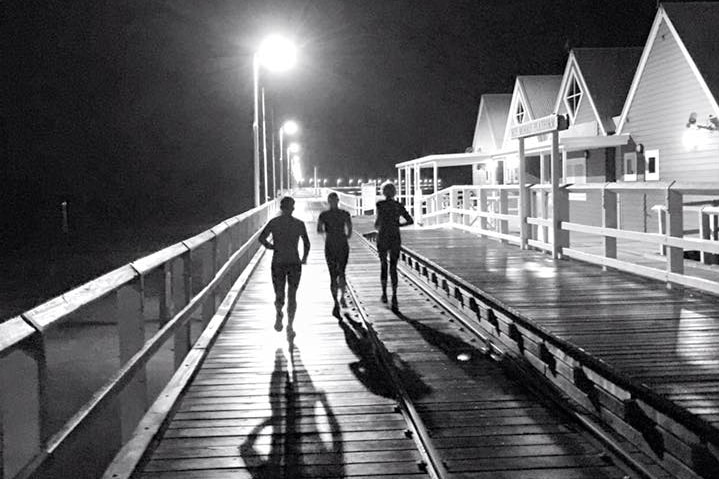 Black and white photo of three women running along a jetty in the early morning