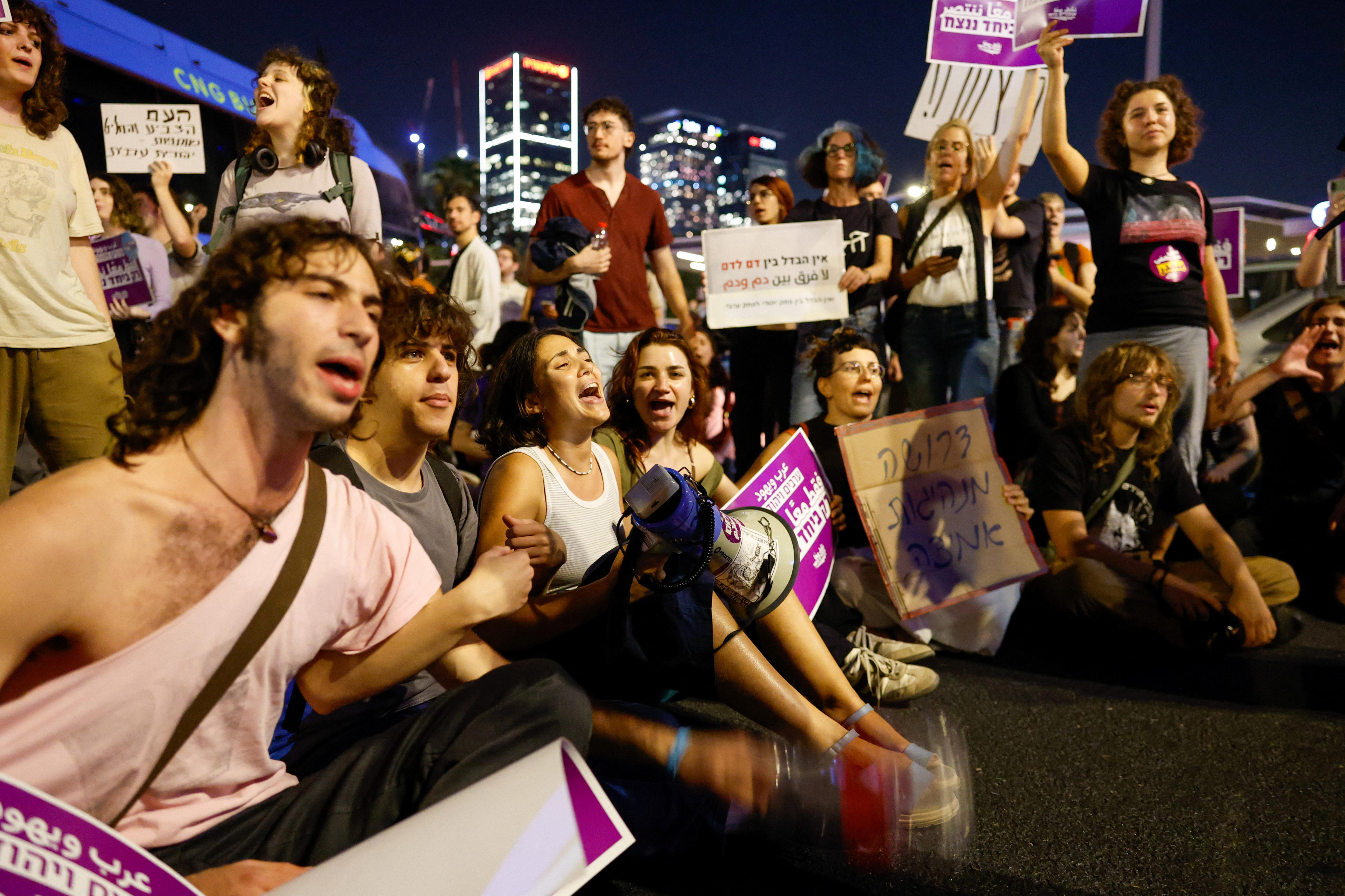 People sit on the ground holding signs with hebrew letters on them.
