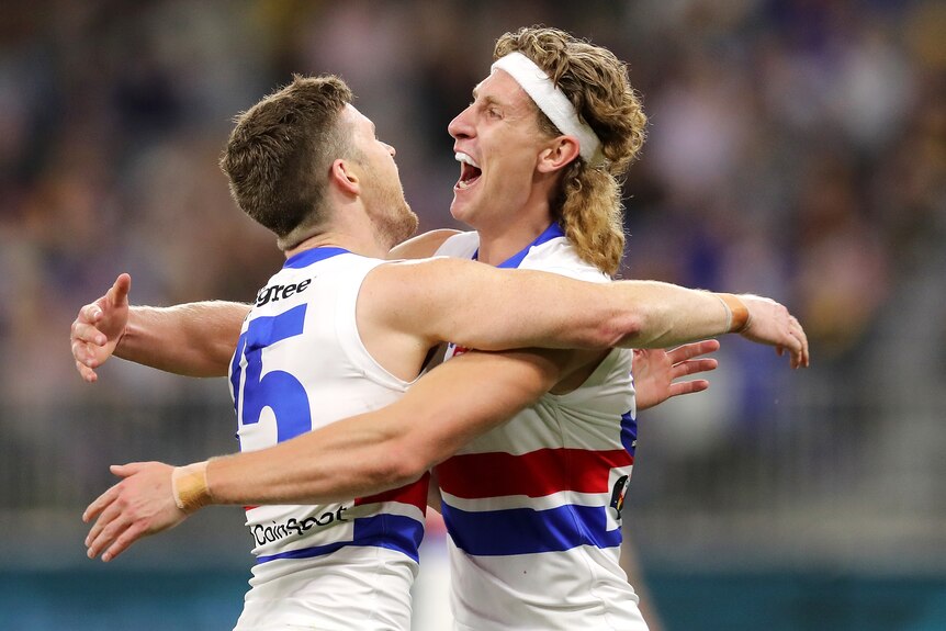 Two Western Bulldogs AFL players embrace as they celebrate a goal.