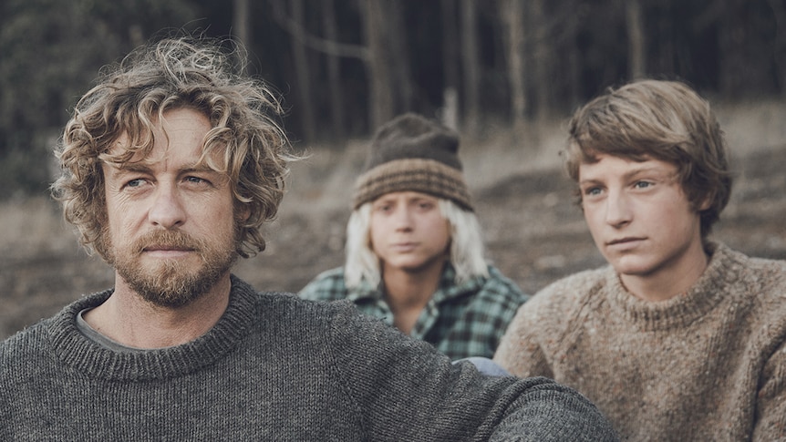 Colour mid-shot photograph of Simon Baker, Ben Spence and Samson Coulter wearing woollen jumpers, near a beach clearing.