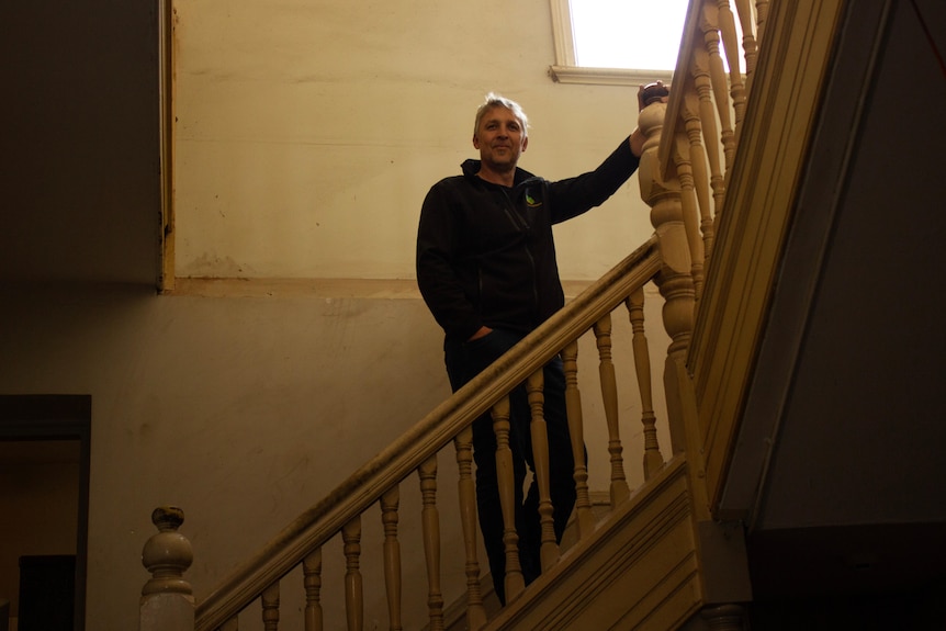 A man wearing black stands on a staircase smiling at the camera 