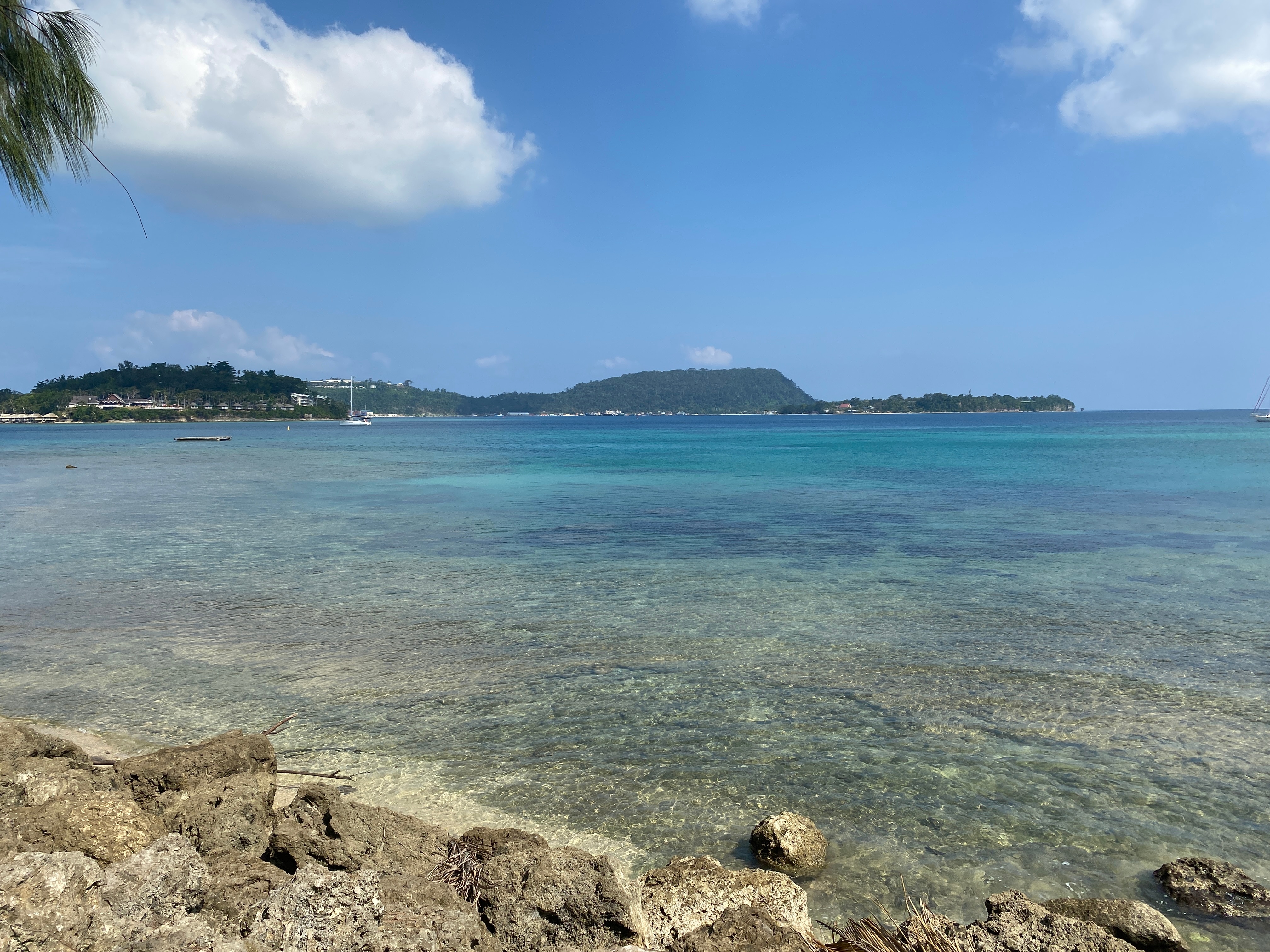 Águas azul-turquesa em uma baía com duas ilhas e um promontório ao fundo.