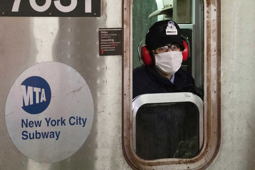 A subway conductor wearing a face mask on a train at a station in New York.