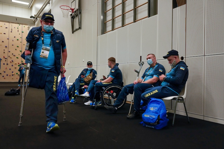 Team Ukraine Invictus Games athletes are shown with crutchs and in wheelchairs inside a gymnasium waiting