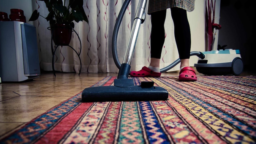 The legs of a woman as she vacuums a red rug.
