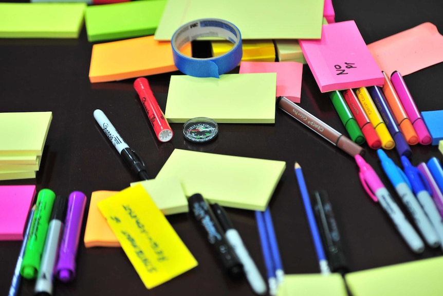 A black table covered with colourful post-it notes and pens.