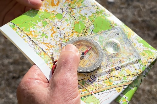A hand holding a compass and a folded map