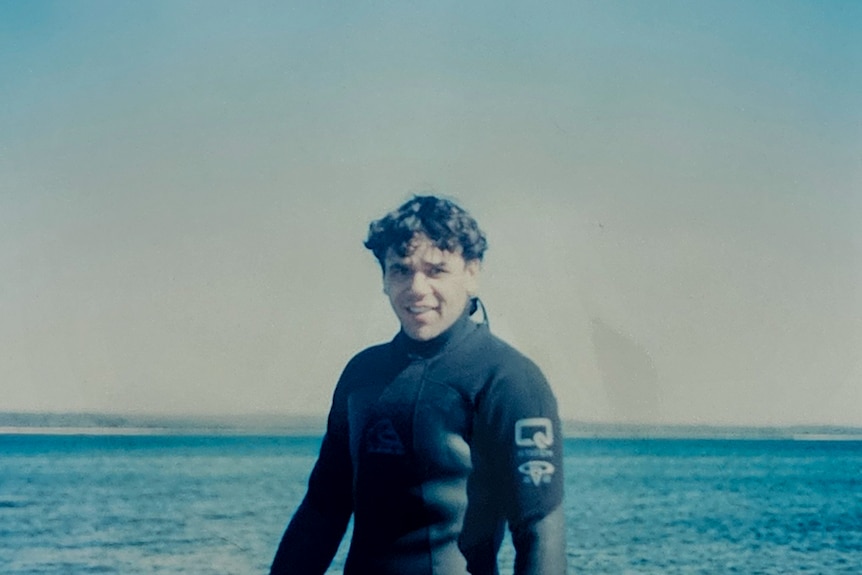 Portrait of young man in a wetsuit standing by the ocean with a gentle smle
