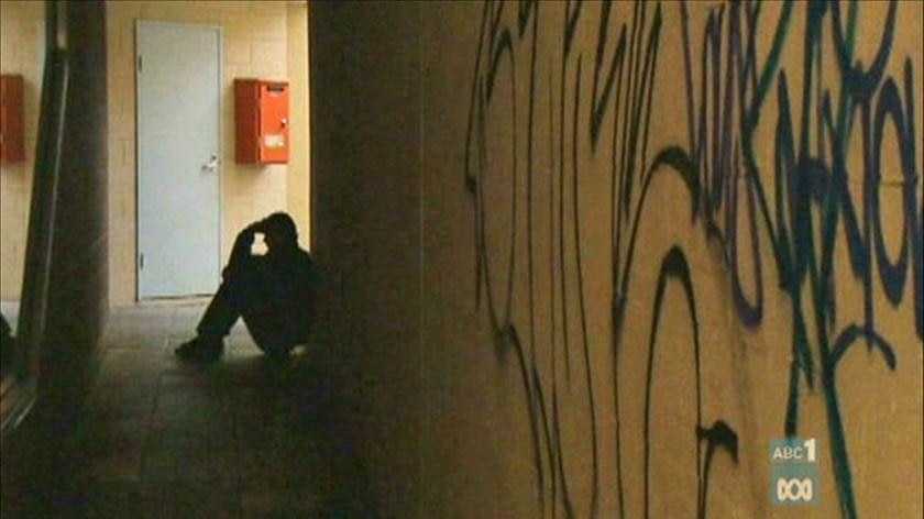 A homeless man sits in the shadows in a hallway