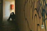 A homeless man sits in the shadows in a hallway
