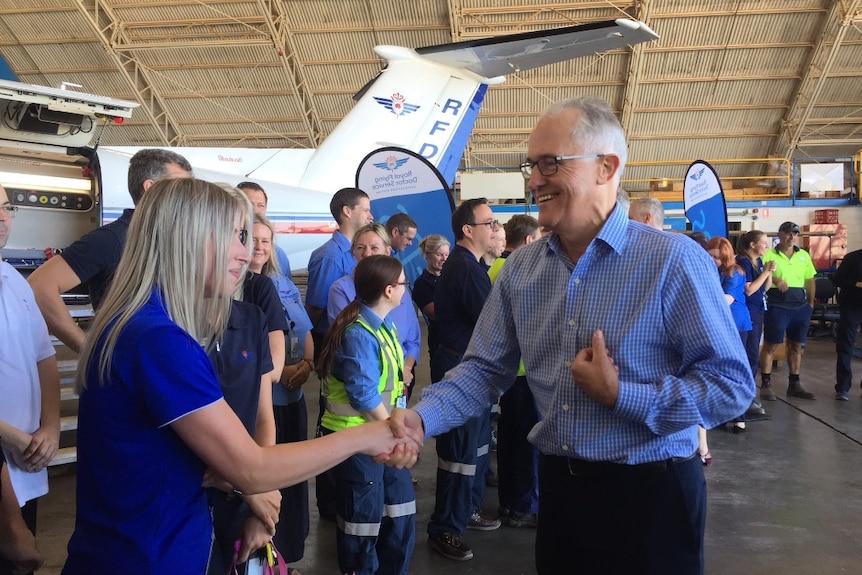 Malcolm Turnbull smiles and reaches a hand out to a woman wearing an RFDS uniform. There is a long line of staff behind her