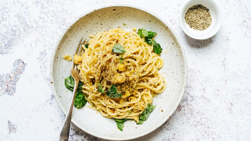 A bowl of spaghetti with chickpea sauce, topped with torn basil, a quick pantry recipe that's vegan.