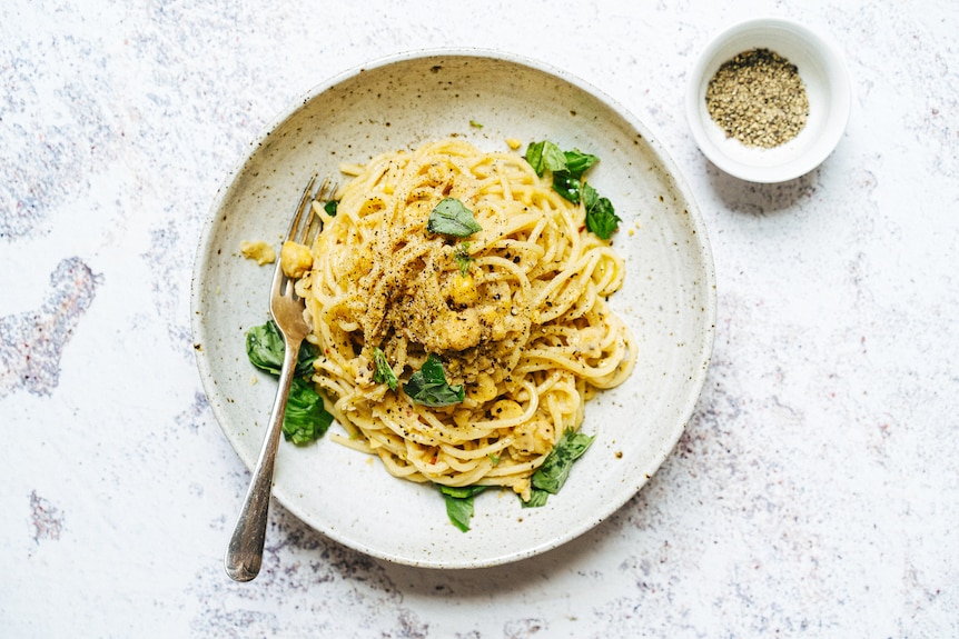 A bowl of spaghetti with chickpea sauce, topped with torn basil, a quick pantry recipe that's vegan.