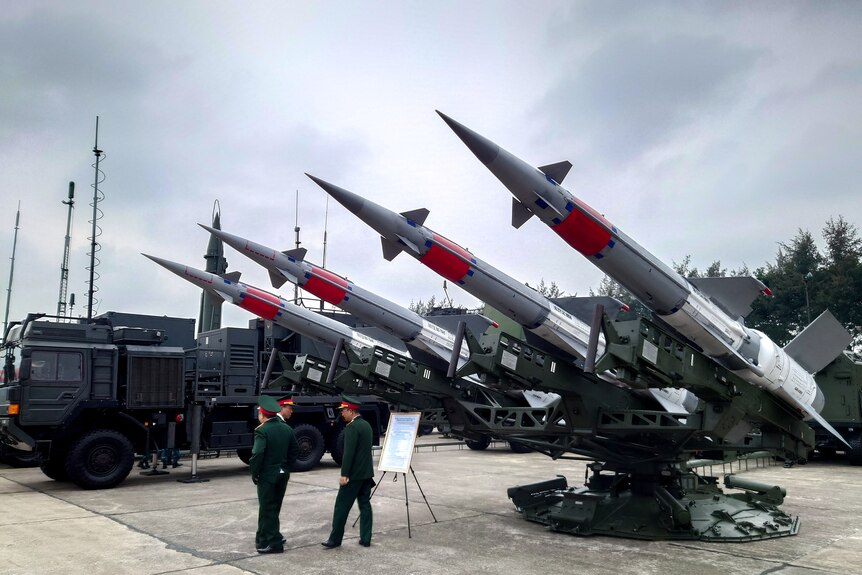 Three military men stand in front of anti-aircraft missiles on display at arms expo held in Hanoi, Vietnam.