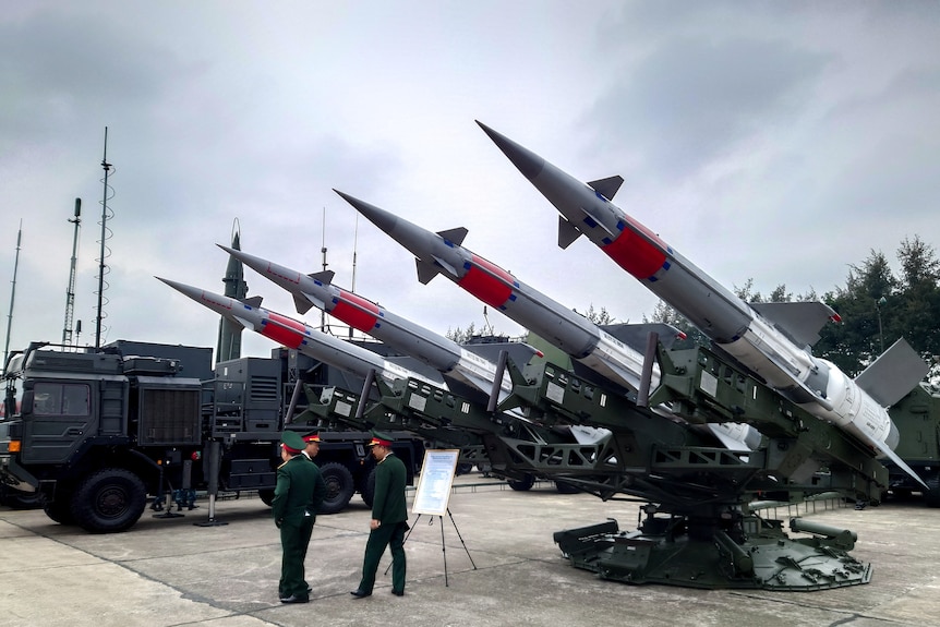 Трое военных стоят перед зенитными ракетами на выставке вооружений в Ханое, Вьетнам.