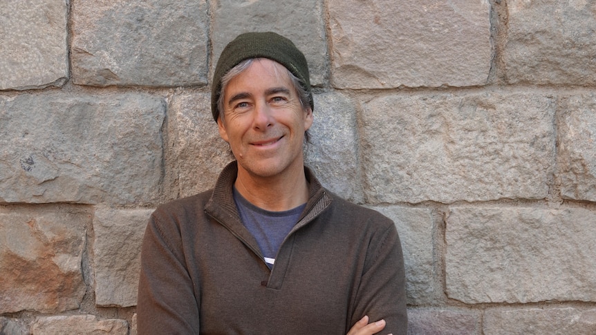 A man in a brown beanie and jumper standing in front of a brick wall