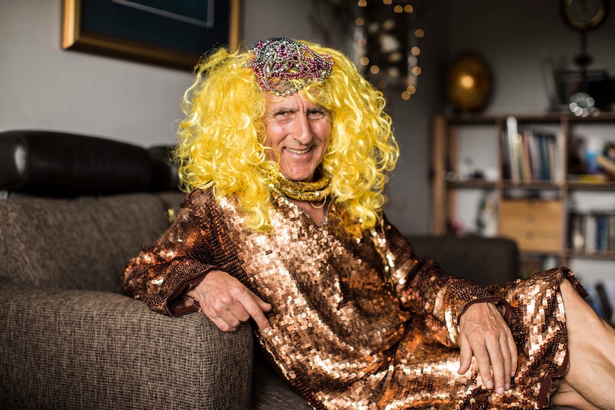 Kim Gotlieb on couch, wearing sequinned bronze dress and yellow-blonde wig.