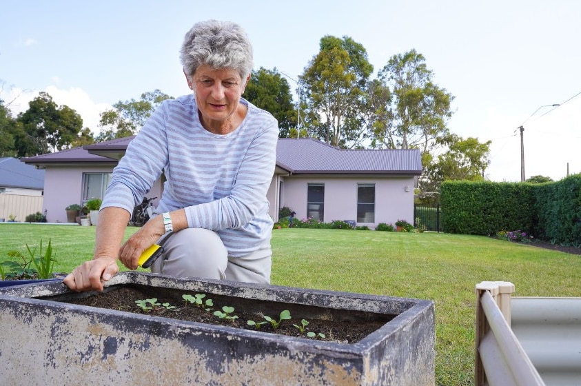 Wendy smiles as she reaches for a raised garden bed in her backyard.