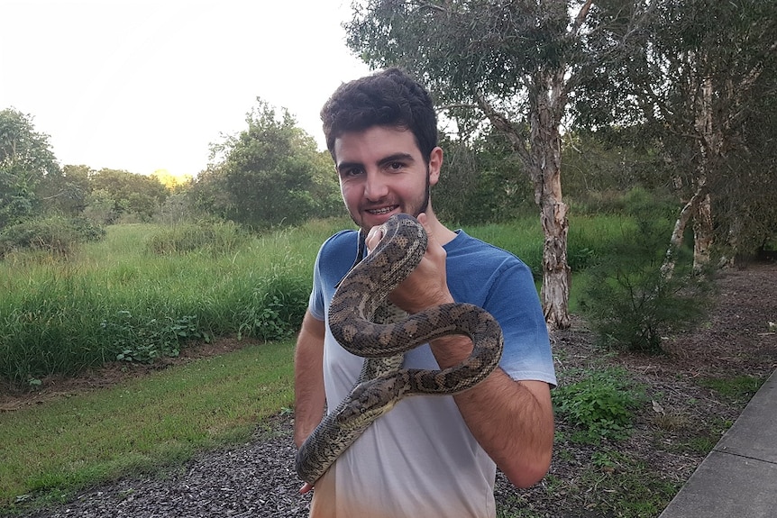 A boy smiling outside, holding a snake