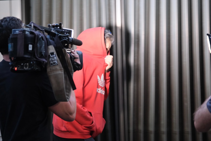 A woman in a hooded jacket covers her face after a court appearance.
