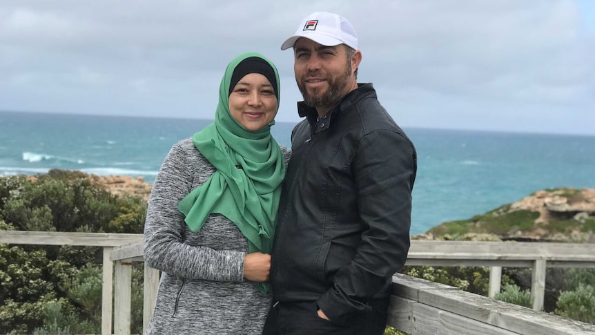 A woman in a headscarf and a man pose by the water