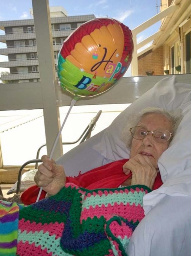 Old lady in pink cardigan on a hospital bed with a balloon