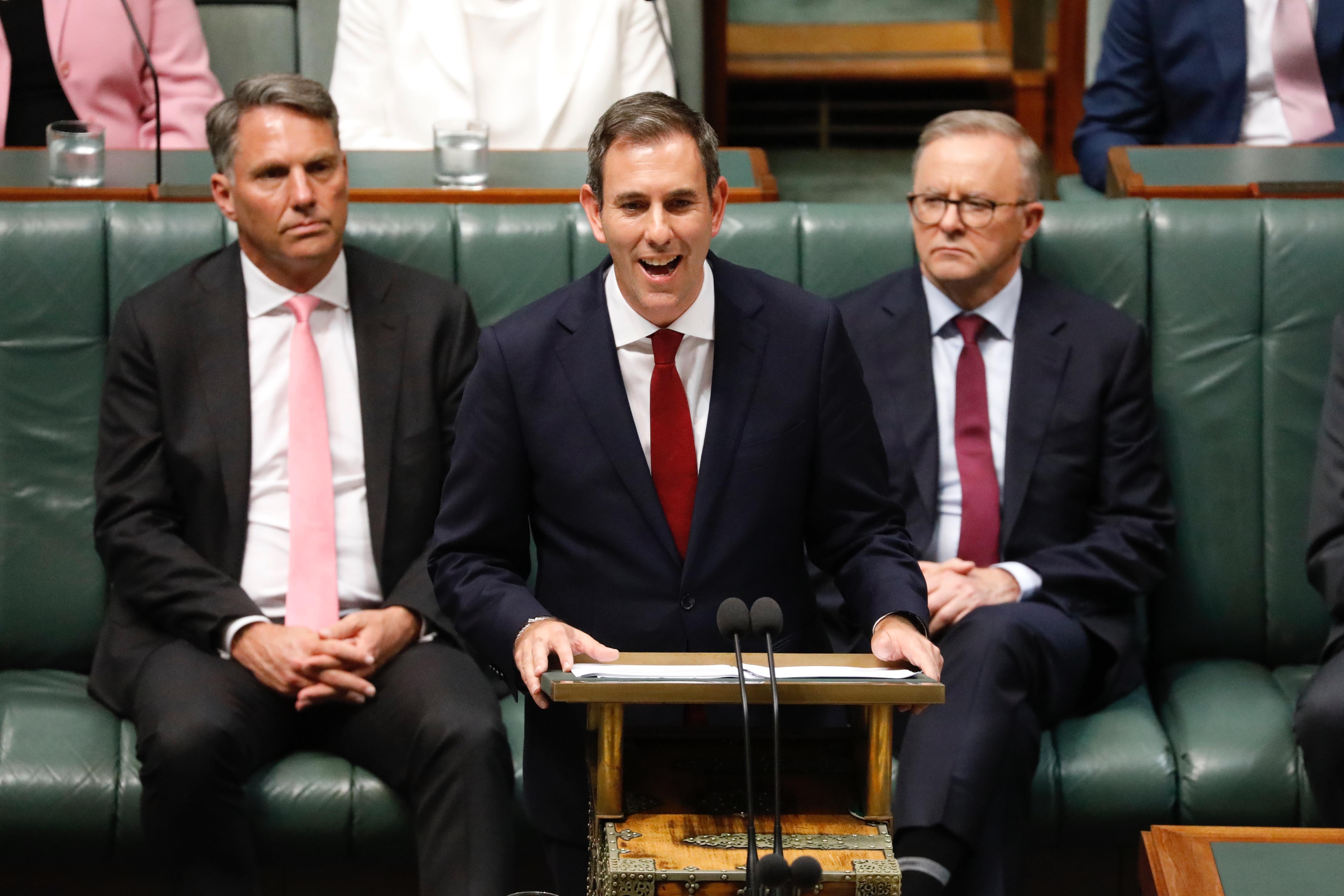 Jim Chalmers at a lecture with two men behind him. 
