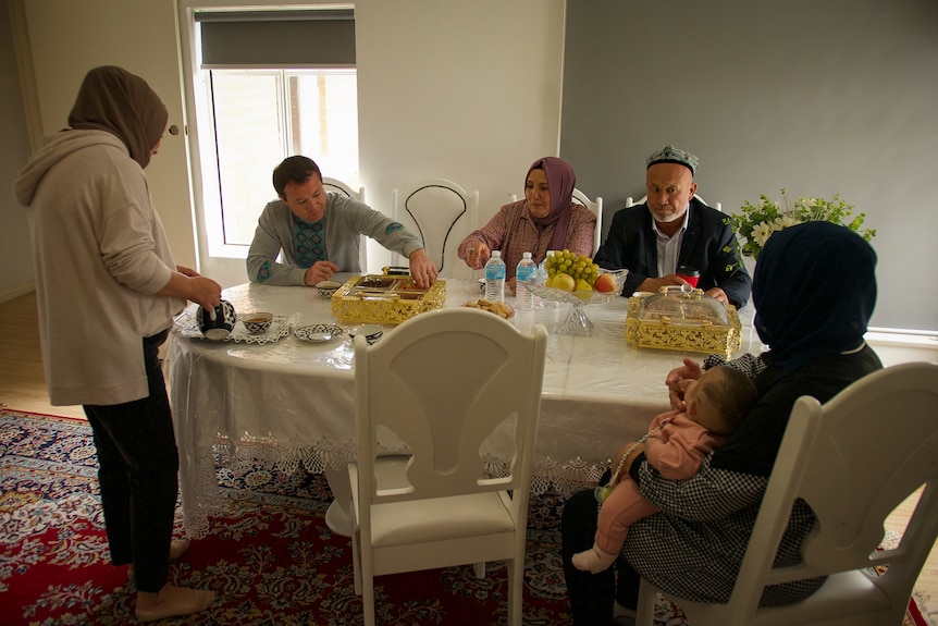 A Uyghur family eats a meal at a white dinner table.
