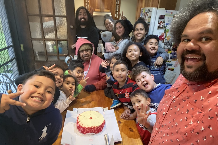 A selfie of a group of young children and adults around a cake. 