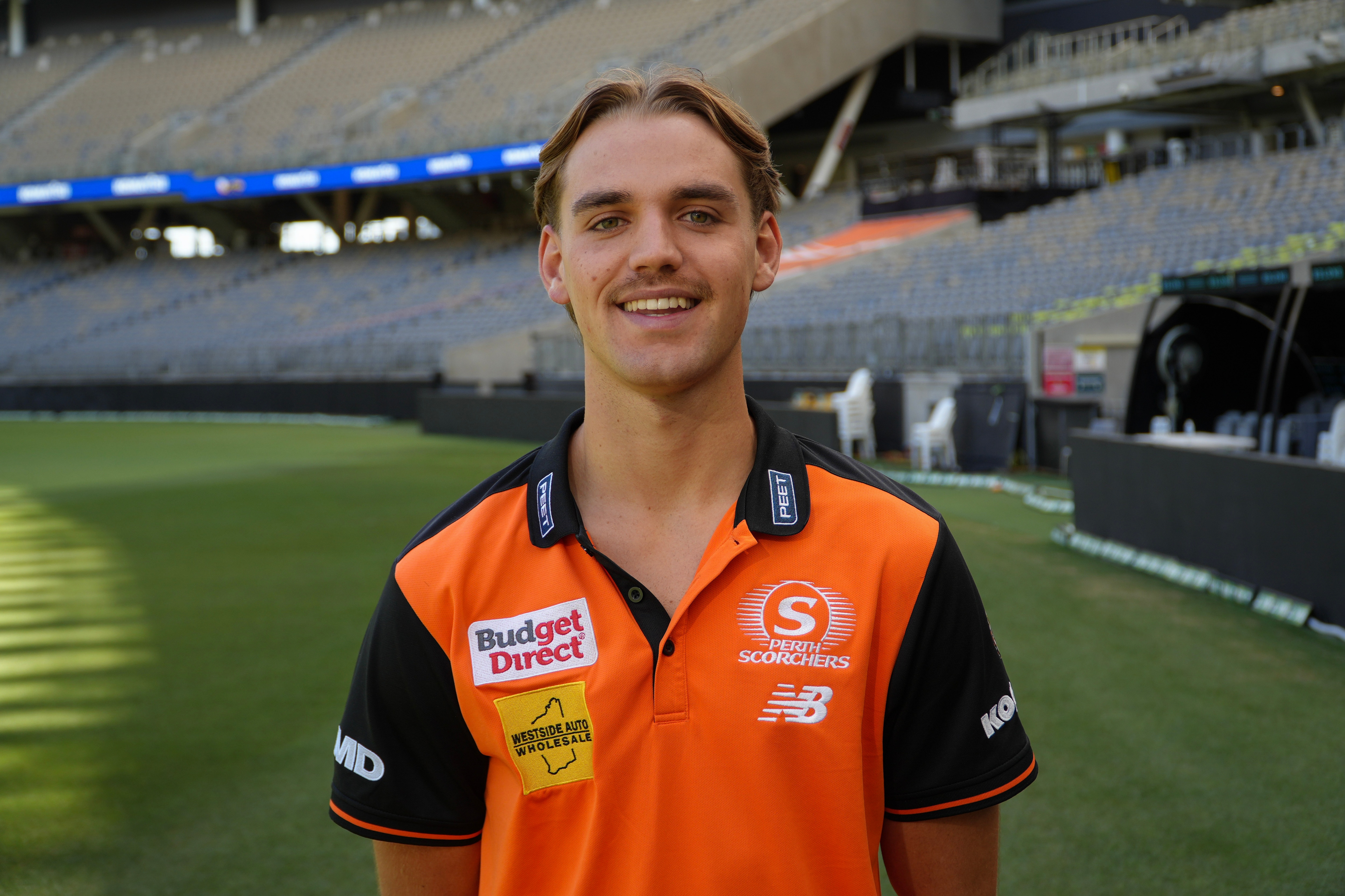 Mahli posa para una foto con su uniforme naranja de Scorchers en el campo de cricket