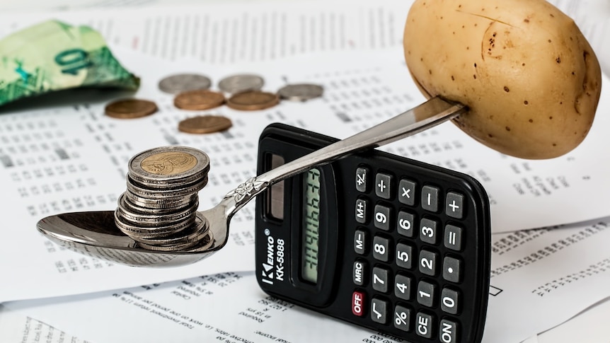 A spoon balanced on a calculator with a potato on one end and coins on the other.