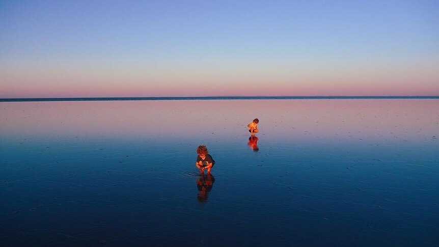 Two young children search for crabs in the shallows of a beach.