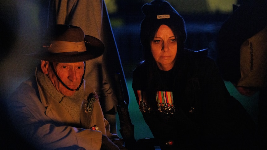 A man in an army uniform and a younger woman stare at a flame.