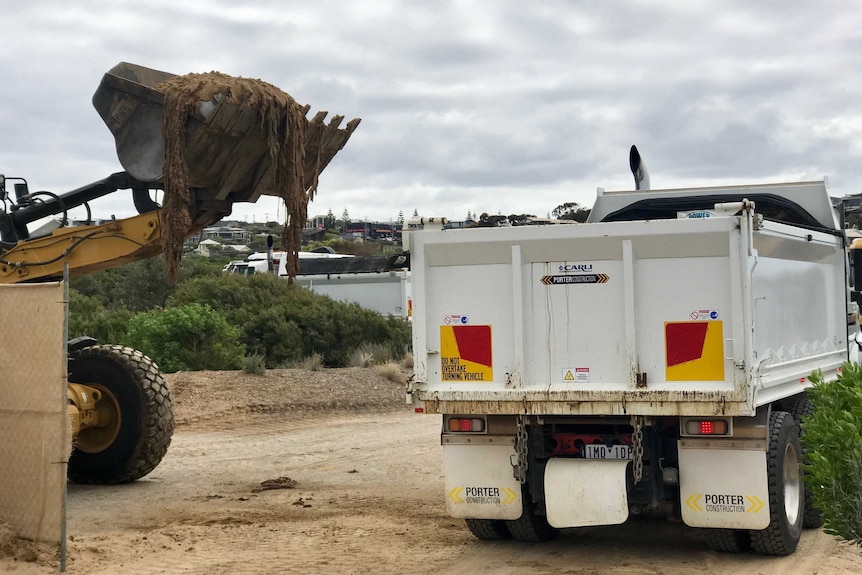 A bulldozer digging in sand next to a truck.