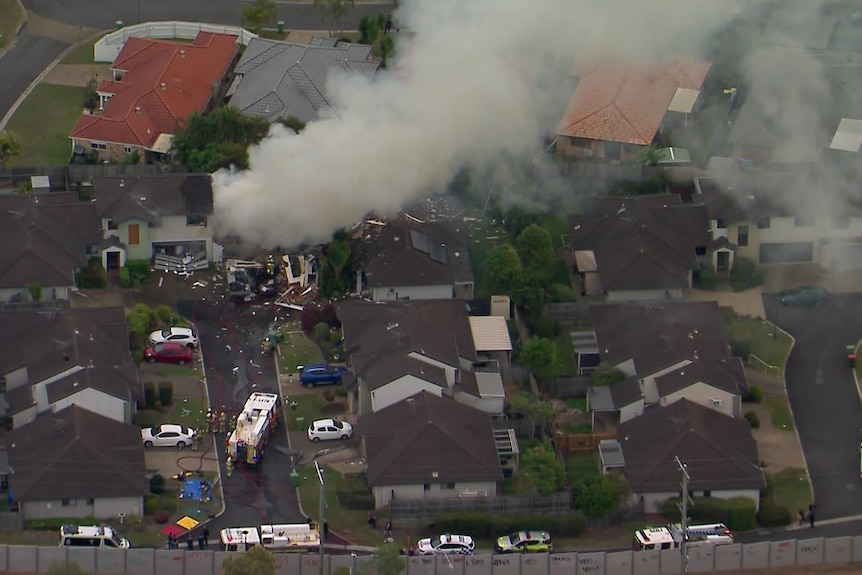 An aerial shot of a Murrumba Downs neighbourhood shows emergency crews on scene and smoke billowing from a home