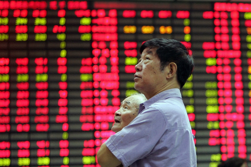 A man stands in front of an electronic stock board at the Shanghai stock market. The board is lit up with red stocks.