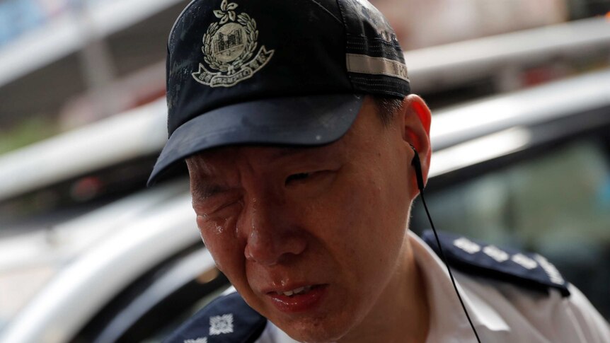 A Hong Kong police officer grimaces with one eye closed and tears running down his face.