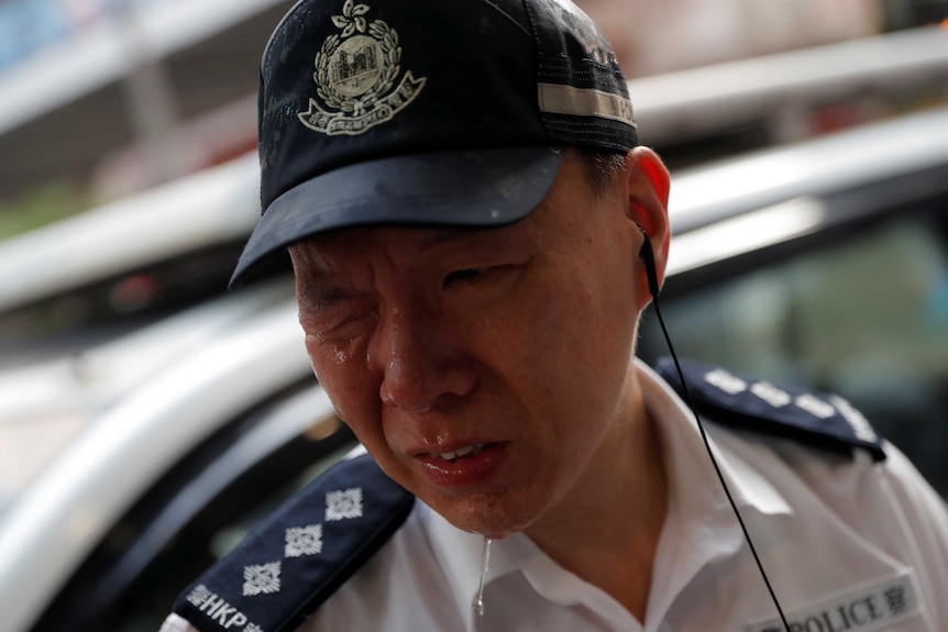 A Hong Kong police officer grimaces with one eye closed and tears running down his face.