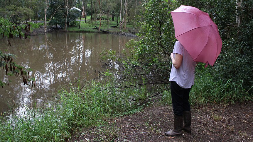 Barbara Rosenberg standing by a lagoon filled with brown water, holding a pink unbrella.
