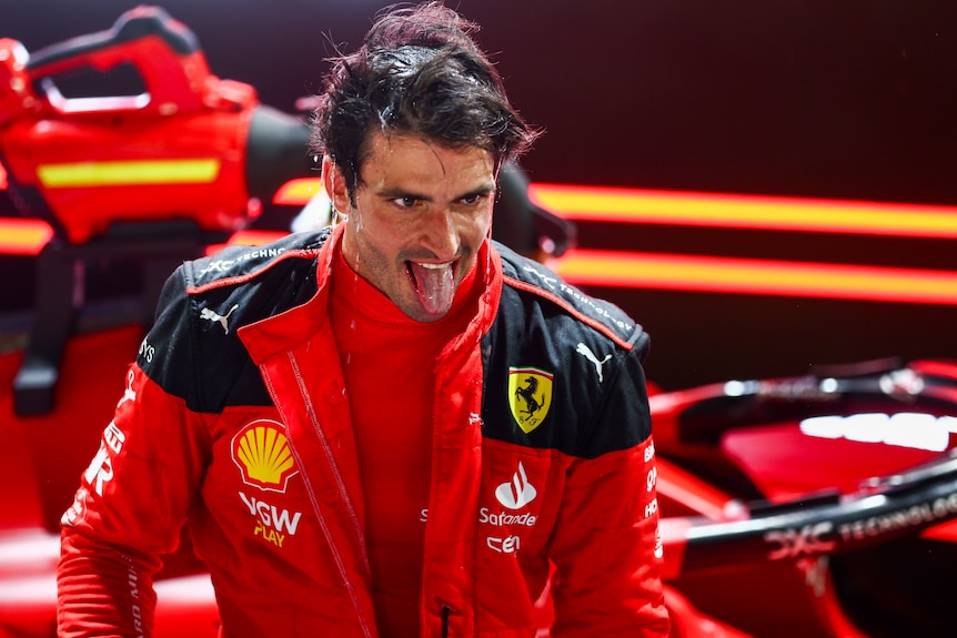 An exhausted F1 driver in a red racing suit, sticks his tongue out in celebration