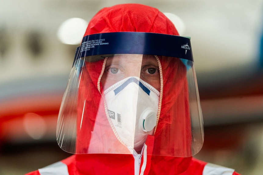 A close-up shot of a male doctor decked out in a PPE face shield and orange hood.