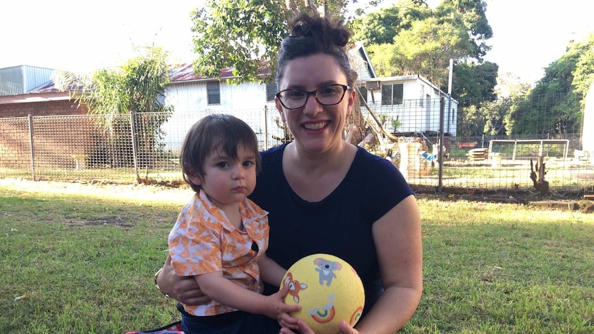 Kate Olivieri sits on a rug holding her son Albert and a children's ball.