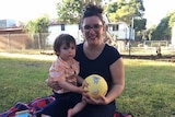 Kate Olivieri sits on a rug holding her son Albert and a children's ball.