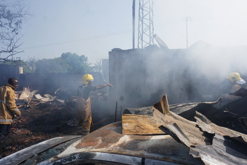 Firefighters work next to burnt wreckage.